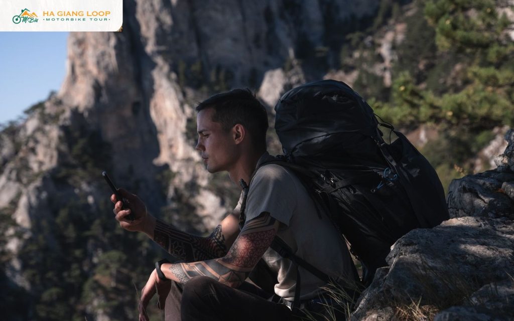 Traveller with a backpack checking phone signal on a rocky Ha Giang Loop mountainside