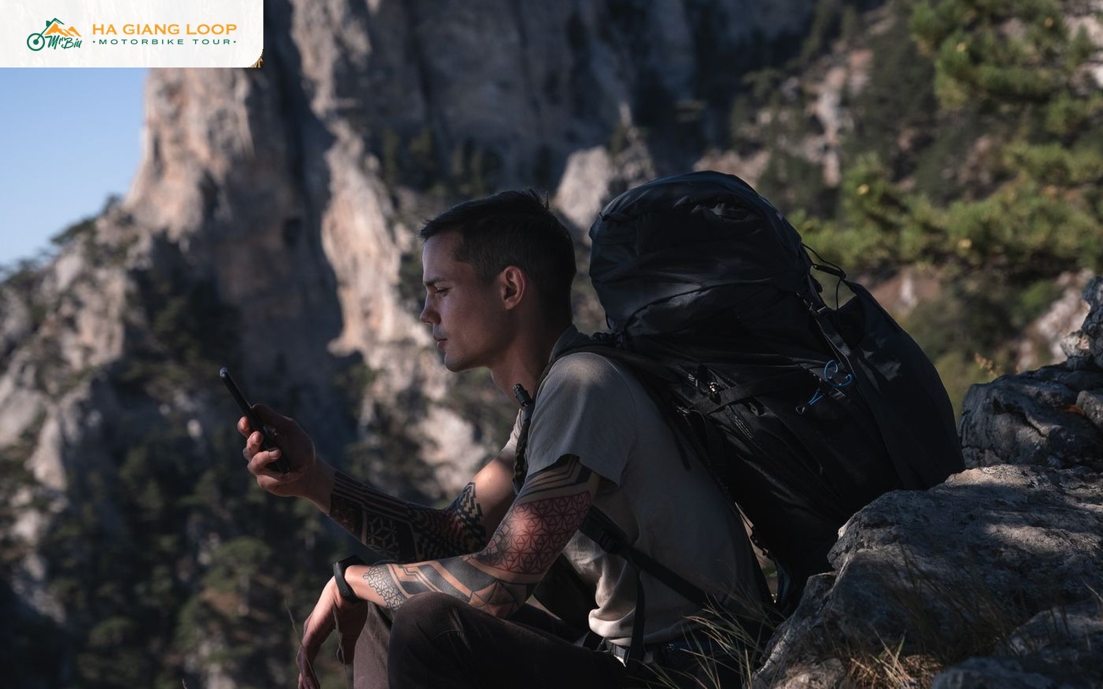 Traveller with a backpack checking phone signal on a rocky Ha Giang Loop mountainside