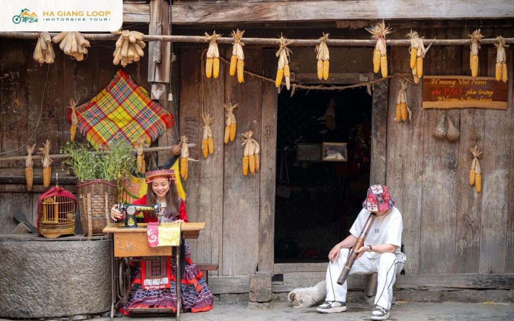 Hmong woman sewing outside a wooden house hung with corn in Pa Vi village near Meo Vac town
