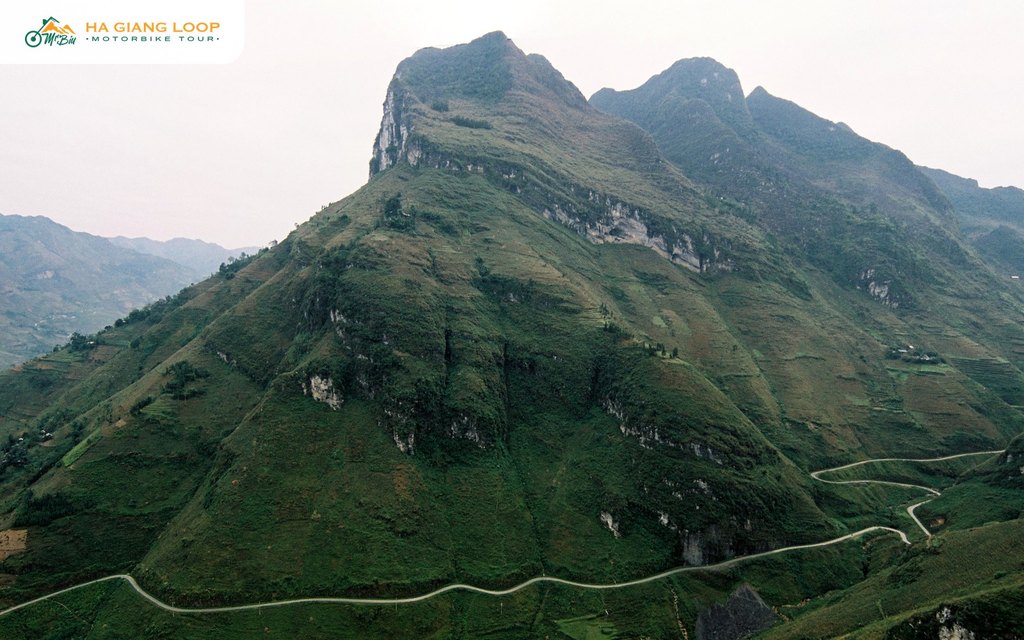Ma Pi Leng pass road winding along a green mountainside in Ha Giang