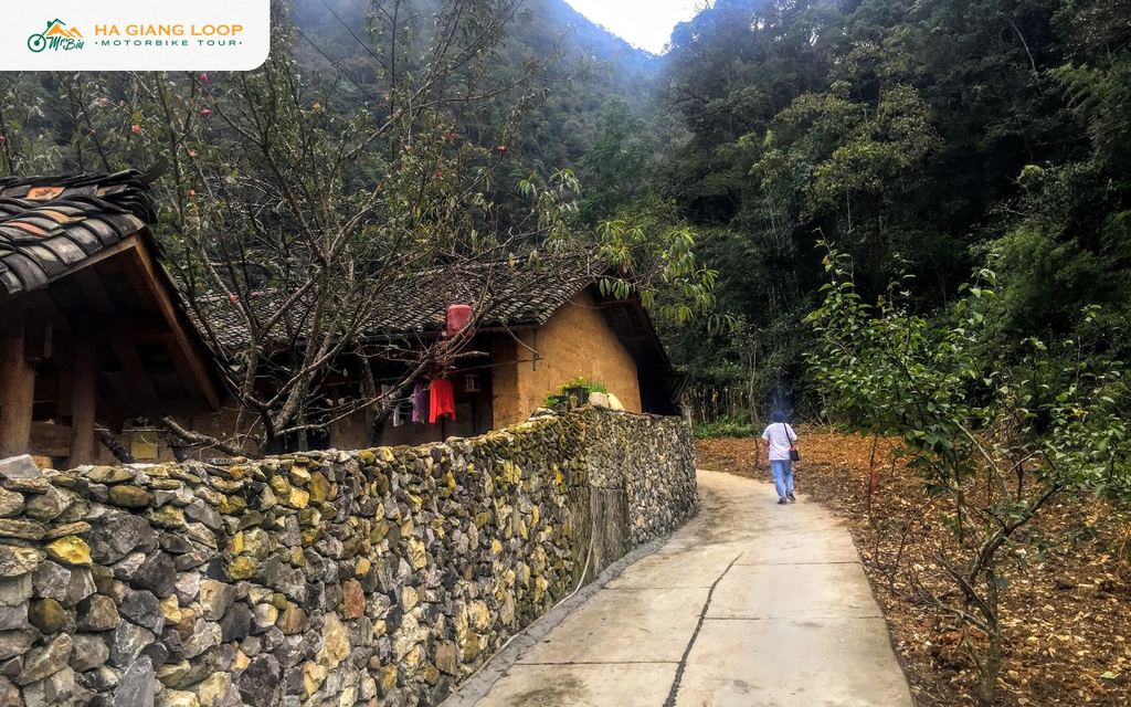 Lane in Lung Cam village with a hand-stacked stone fence and an earthen house