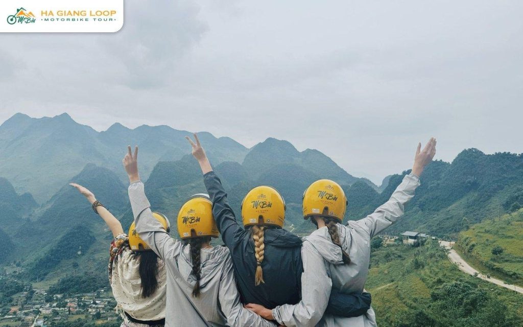 Three passengers in yellow helmets with arms open at a Ha Giang viewpoint